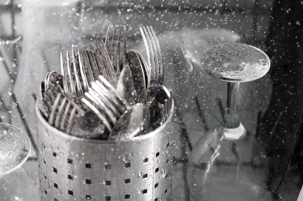 Forks in a basket being washed next to glasses
