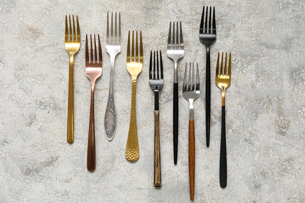 Gold, copper, black, and silver forks on a marble background