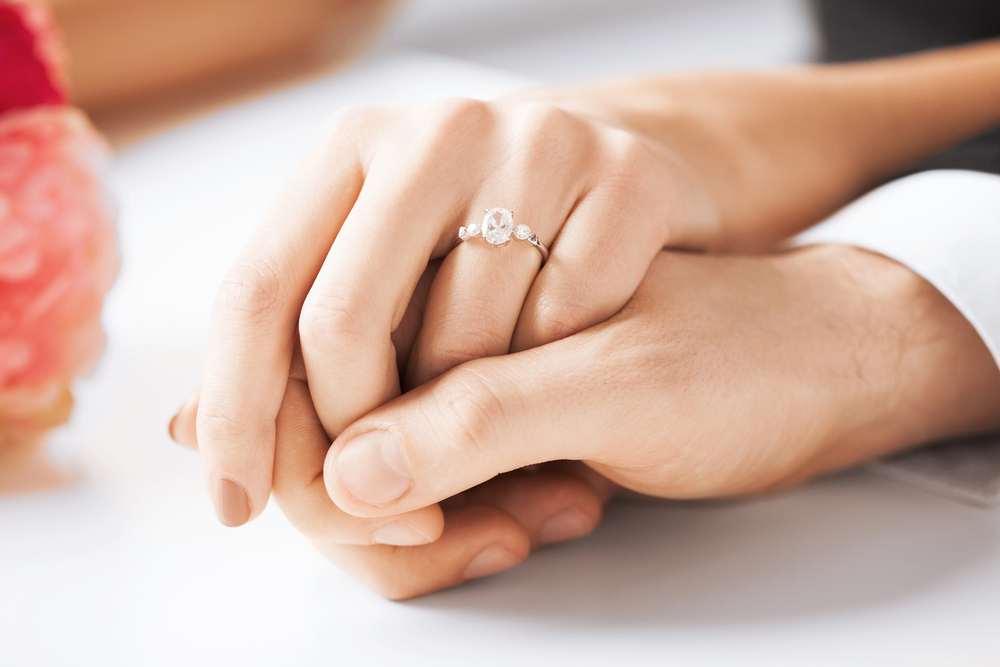 A couple holding hands, ring on her finger