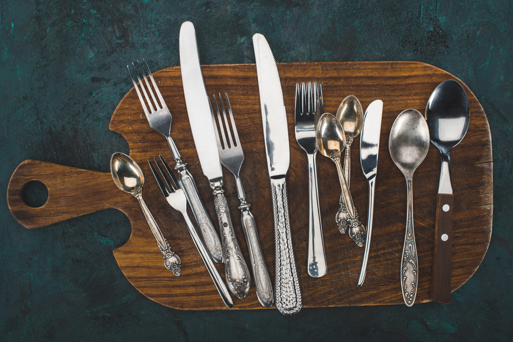 A handful of silver forks and knives on a butcher block